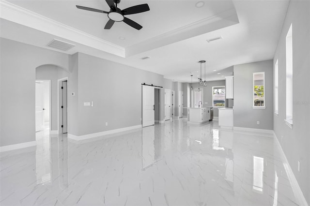 unfurnished living room with sink, ceiling fan, a tray ceiling, crown molding, and a barn door