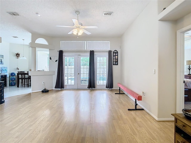 living room with a textured ceiling, ceiling fan, light hardwood / wood-style floors, and french doors