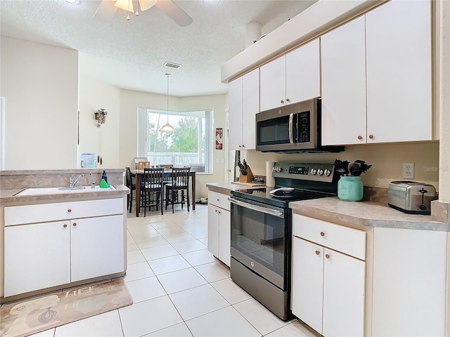 kitchen featuring appliances with stainless steel finishes, light tile patterned flooring, a textured ceiling, pendant lighting, and white cabinets