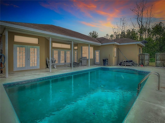 pool at dusk with a grill, french doors, and a patio