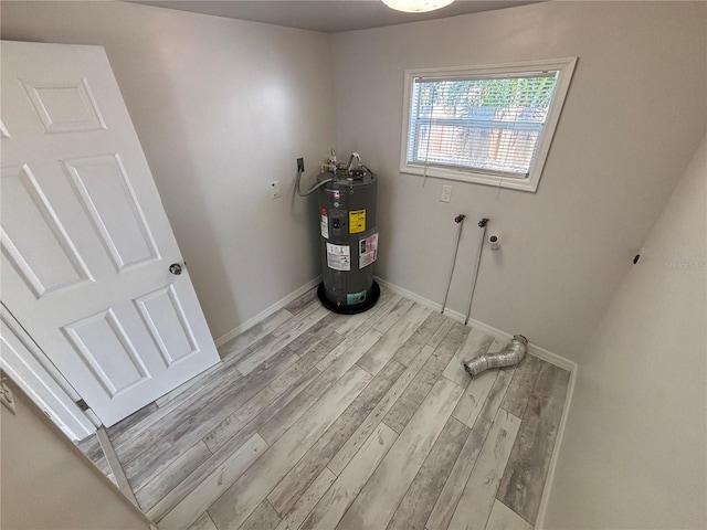 clothes washing area with water heater and light hardwood / wood-style flooring