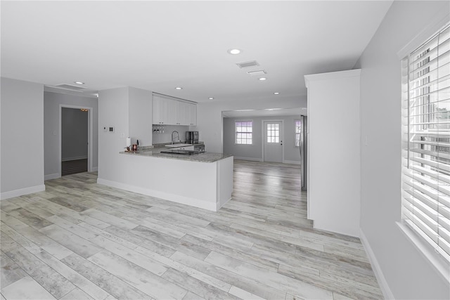 kitchen with dark stone counters, kitchen peninsula, sink, white cabinetry, and light wood-type flooring