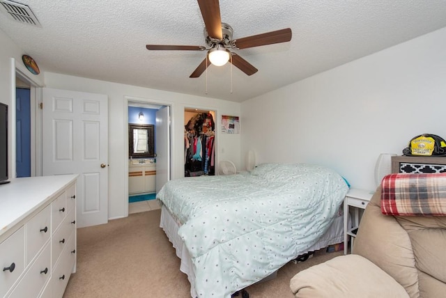 bedroom featuring light carpet, ceiling fan, a walk in closet, connected bathroom, and a closet