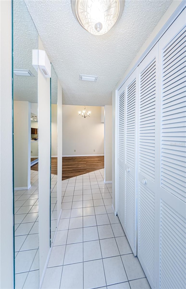 hall featuring light tile patterned flooring, a chandelier, and a textured ceiling