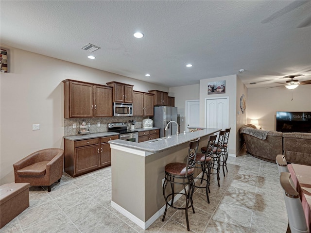 kitchen with a center island with sink, stainless steel appliances, sink, decorative backsplash, and a kitchen breakfast bar