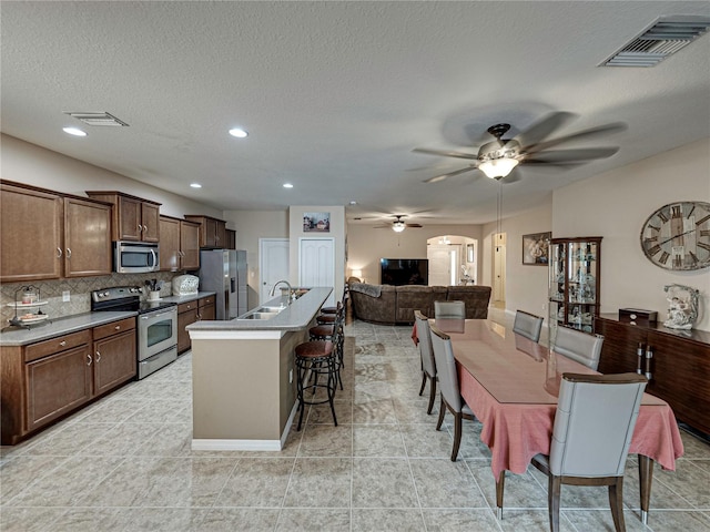 kitchen with stainless steel appliances, backsplash, sink, a breakfast bar area, and a kitchen island with sink