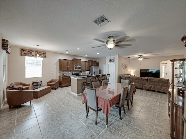 dining area featuring light tile patterned flooring, ceiling fan with notable chandelier, and a textured ceiling