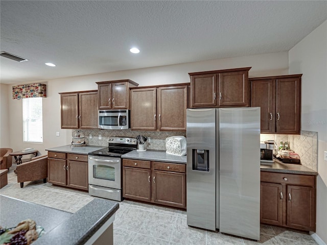 kitchen featuring tasteful backsplash, a textured ceiling, light tile patterned flooring, and stainless steel appliances