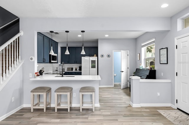 kitchen featuring light hardwood / wood-style floors, a breakfast bar, kitchen peninsula, white fridge, and pendant lighting