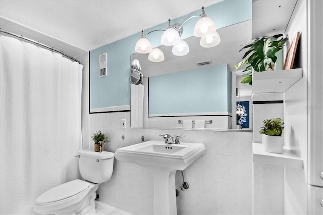 bathroom featuring toilet, a wainscoted wall, a sink, visible vents, and tile walls