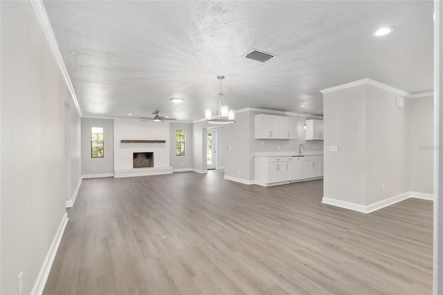 unfurnished living room featuring a fireplace, ceiling fan with notable chandelier, light hardwood / wood-style flooring, and crown molding