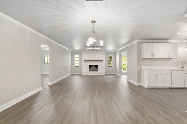 unfurnished living room featuring a fireplace, wood-type flooring, crown molding, and a notable chandelier