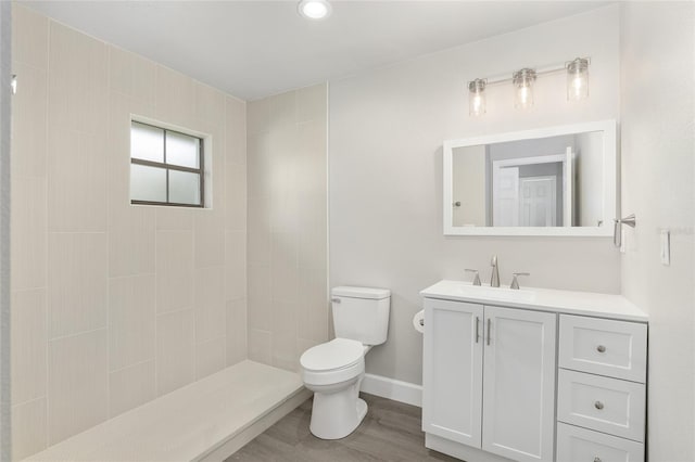 bathroom with tiled shower, hardwood / wood-style floors, vanity, and toilet