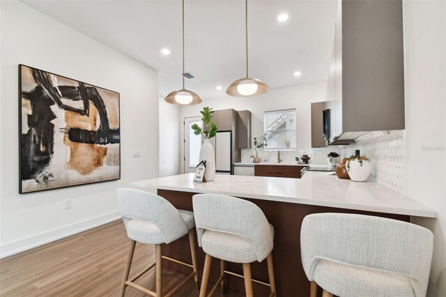 kitchen with wood-type flooring, kitchen peninsula, decorative backsplash, a breakfast bar, and decorative light fixtures