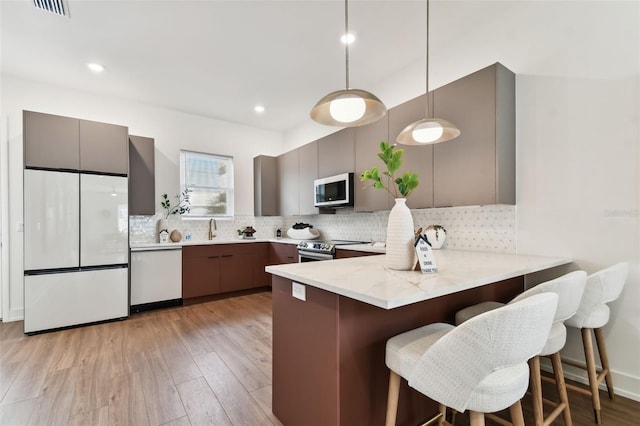 kitchen featuring stainless steel appliances, kitchen peninsula, hanging light fixtures, a breakfast bar area, and light hardwood / wood-style flooring