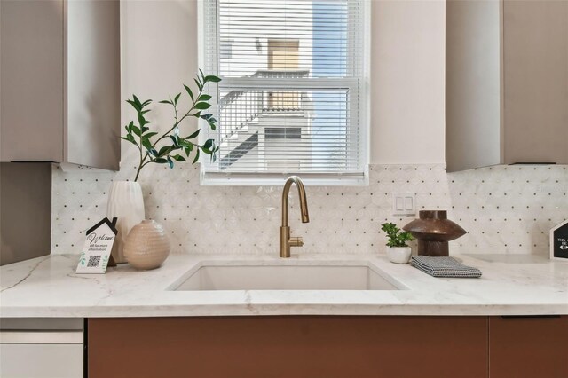 interior details with tasteful backsplash, light stone countertops, and sink