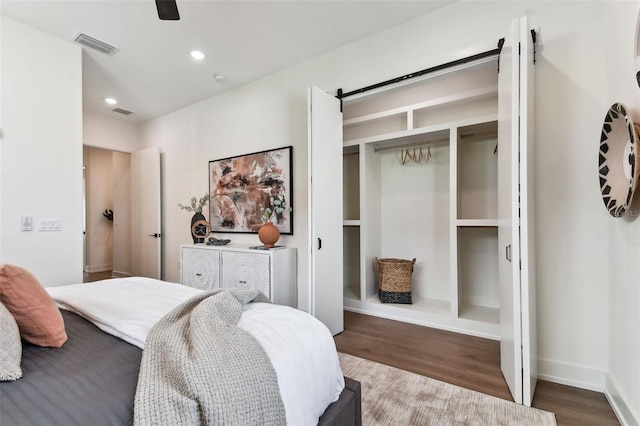 bedroom with a barn door, ceiling fan, dark hardwood / wood-style floors, and a closet