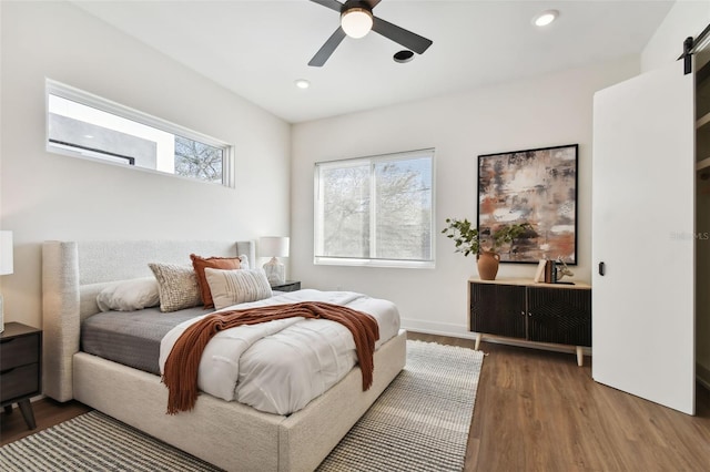 bedroom with hardwood / wood-style flooring, a barn door, and ceiling fan