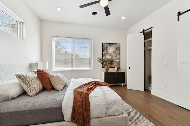 bedroom featuring dark hardwood / wood-style flooring, multiple windows, a barn door, and ceiling fan