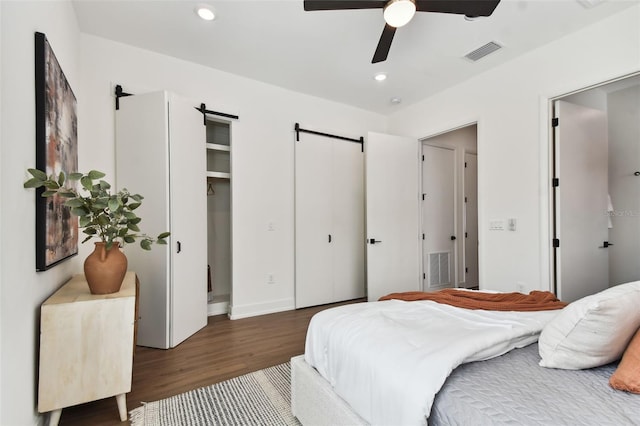 bedroom featuring a barn door, ceiling fan, and dark hardwood / wood-style flooring