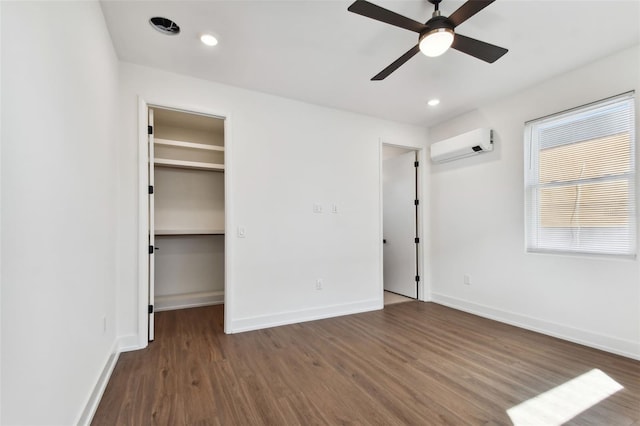 unfurnished bedroom featuring a wall unit AC, ceiling fan, a walk in closet, and dark hardwood / wood-style flooring