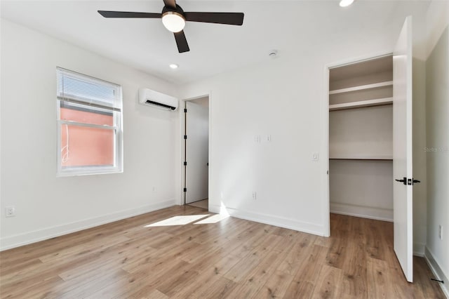 unfurnished bedroom with light hardwood / wood-style floors, an AC wall unit, ceiling fan, and a walk in closet