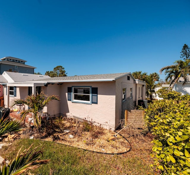 view of side of property with stucco siding, cooling unit, and a shingled roof