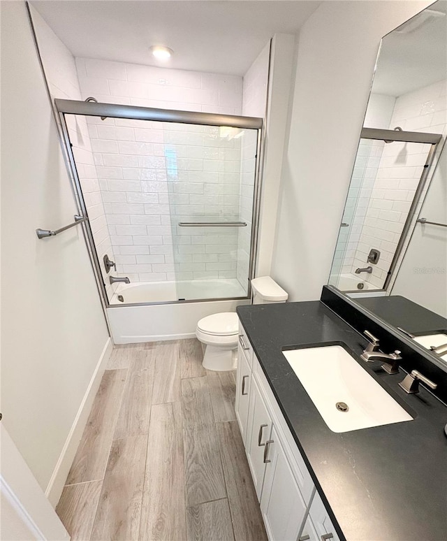 full bathroom featuring toilet, vanity, bath / shower combo with glass door, and hardwood / wood-style flooring