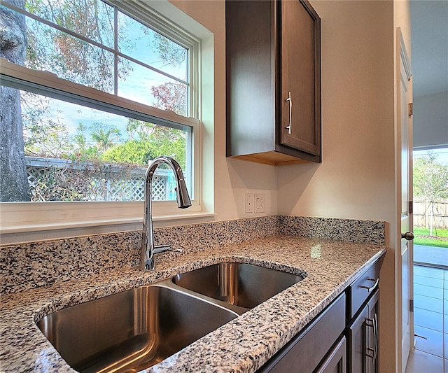 kitchen featuring light stone countertops, tile patterned flooring, sink, and dark brown cabinetry