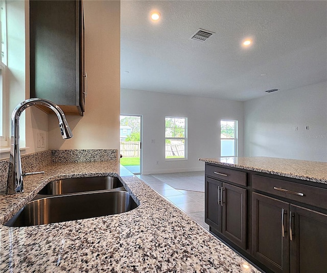 kitchen with light stone countertops, sink, dark brown cabinetry, and a textured ceiling