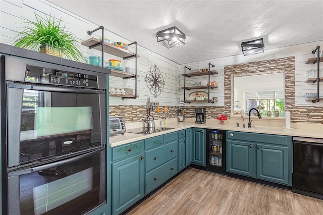 kitchen with black appliances, blue cabinetry, sink, beverage cooler, and light hardwood / wood-style flooring