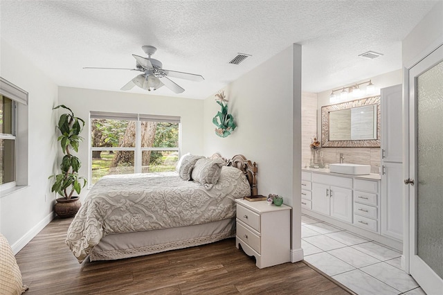 bedroom featuring a textured ceiling, ensuite bathroom, light hardwood / wood-style floors, and ceiling fan