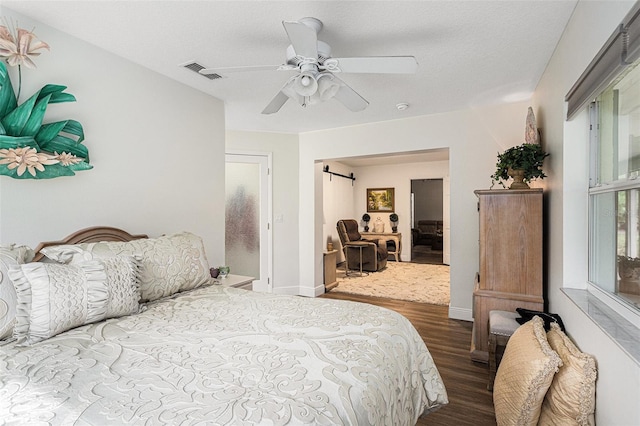 bedroom featuring a barn door, ceiling fan, a textured ceiling, and hardwood / wood-style floors