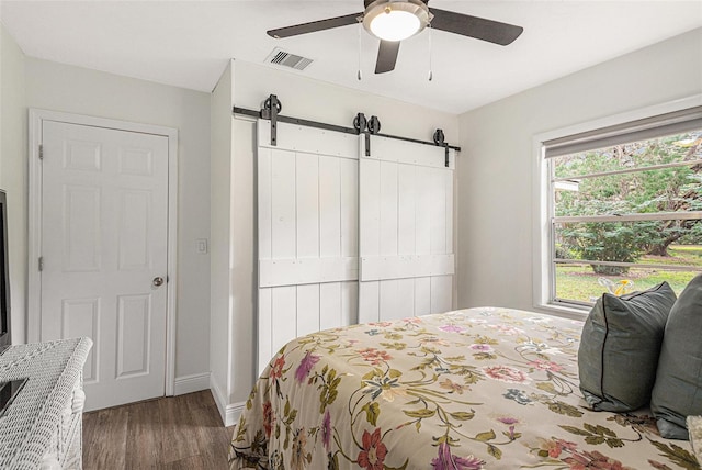 bedroom with a barn door, ceiling fan, multiple windows, and dark hardwood / wood-style floors