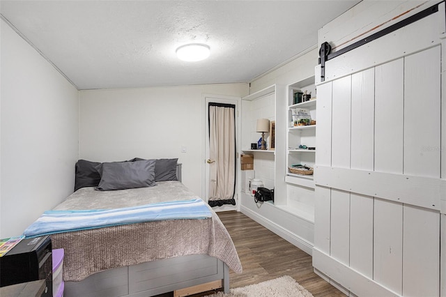 bedroom with hardwood / wood-style floors, a barn door, a textured ceiling, and lofted ceiling