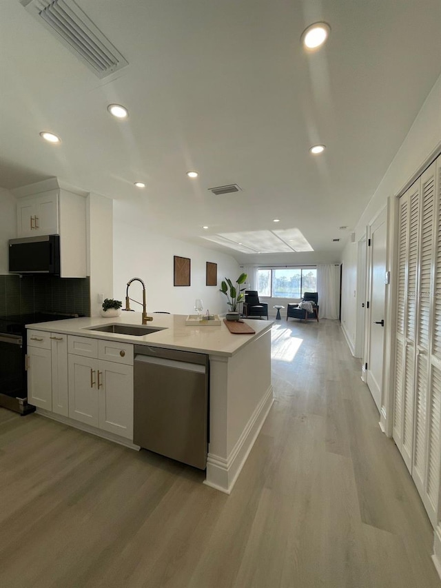 kitchen featuring white cabinets, sink, light wood-type flooring, appliances with stainless steel finishes, and tasteful backsplash