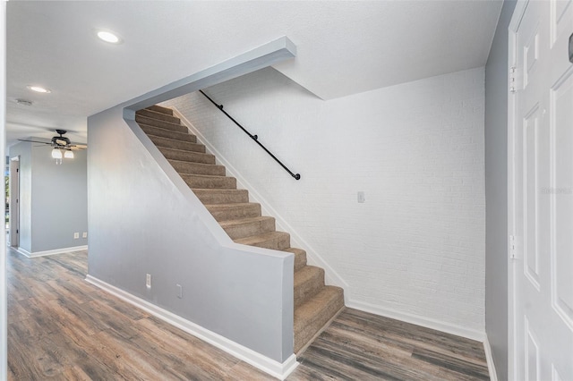 stairs with hardwood / wood-style floors, ceiling fan, and brick wall