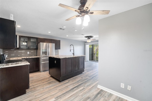 kitchen featuring black range oven, light stone counters, light hardwood / wood-style flooring, stainless steel refrigerator with ice dispenser, and a center island with sink