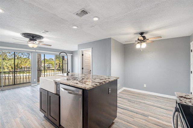 kitchen with light stone countertops, stainless steel appliances, a textured ceiling, a kitchen island with sink, and light wood-type flooring