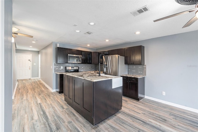 kitchen with appliances with stainless steel finishes, light hardwood / wood-style floors, dark brown cabinets, and a center island with sink