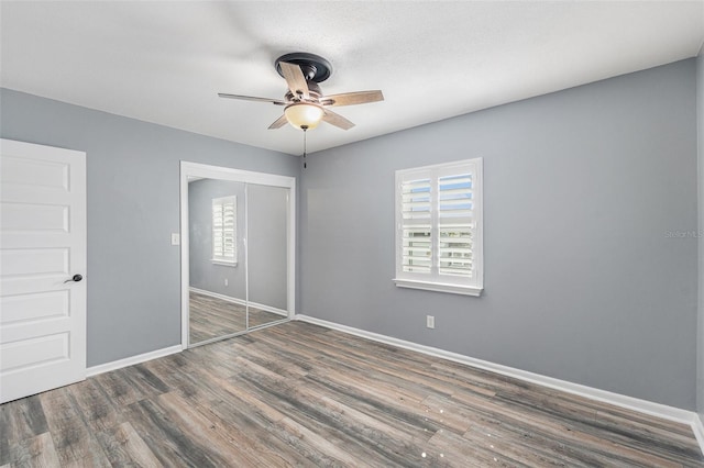 unfurnished bedroom with a closet, ceiling fan, multiple windows, and dark hardwood / wood-style flooring