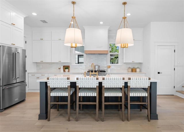 kitchen with decorative light fixtures, high quality fridge, and an island with sink