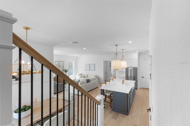 interior space with hanging light fixtures, a breakfast bar area, an island with sink, stainless steel refrigerator, and light wood-type flooring