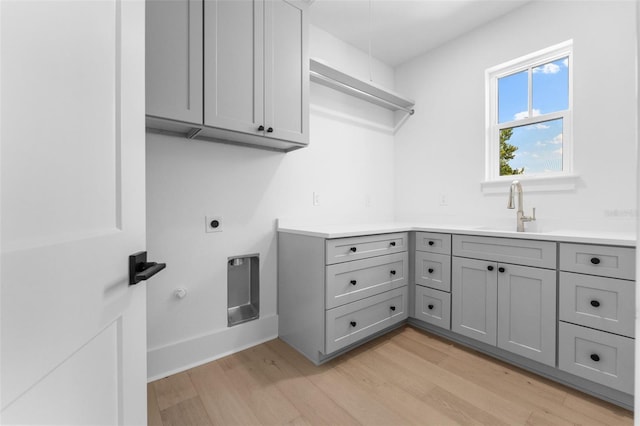 clothes washing area with electric dryer hookup, cabinets, sink, and light hardwood / wood-style floors