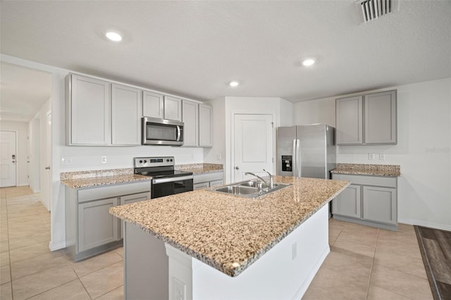 kitchen with gray cabinetry, a center island with sink, appliances with stainless steel finishes, light stone countertops, and sink