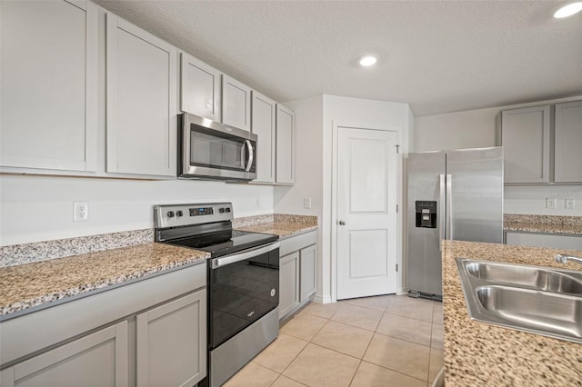 kitchen with a textured ceiling, sink, light tile patterned floors, and stainless steel appliances