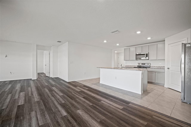 kitchen featuring stainless steel appliances, gray cabinetry, a kitchen island with sink, and light hardwood / wood-style flooring