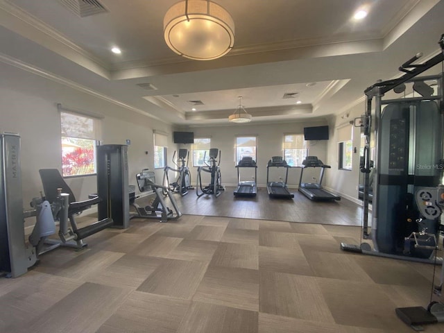 exercise room with ornamental molding, dark hardwood / wood-style flooring, a raised ceiling, and a healthy amount of sunlight