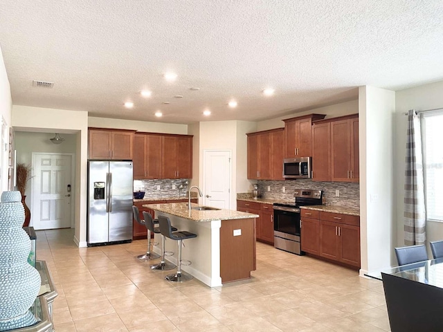 kitchen with light stone countertops, a breakfast bar, stainless steel appliances, a kitchen island with sink, and sink