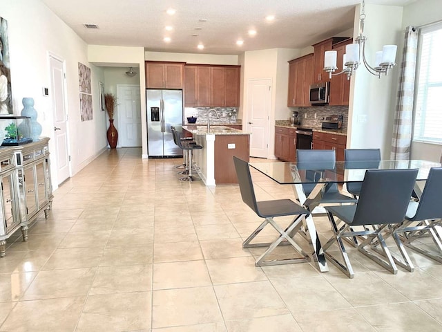 kitchen featuring a kitchen bar, backsplash, a kitchen island with sink, appliances with stainless steel finishes, and light stone counters